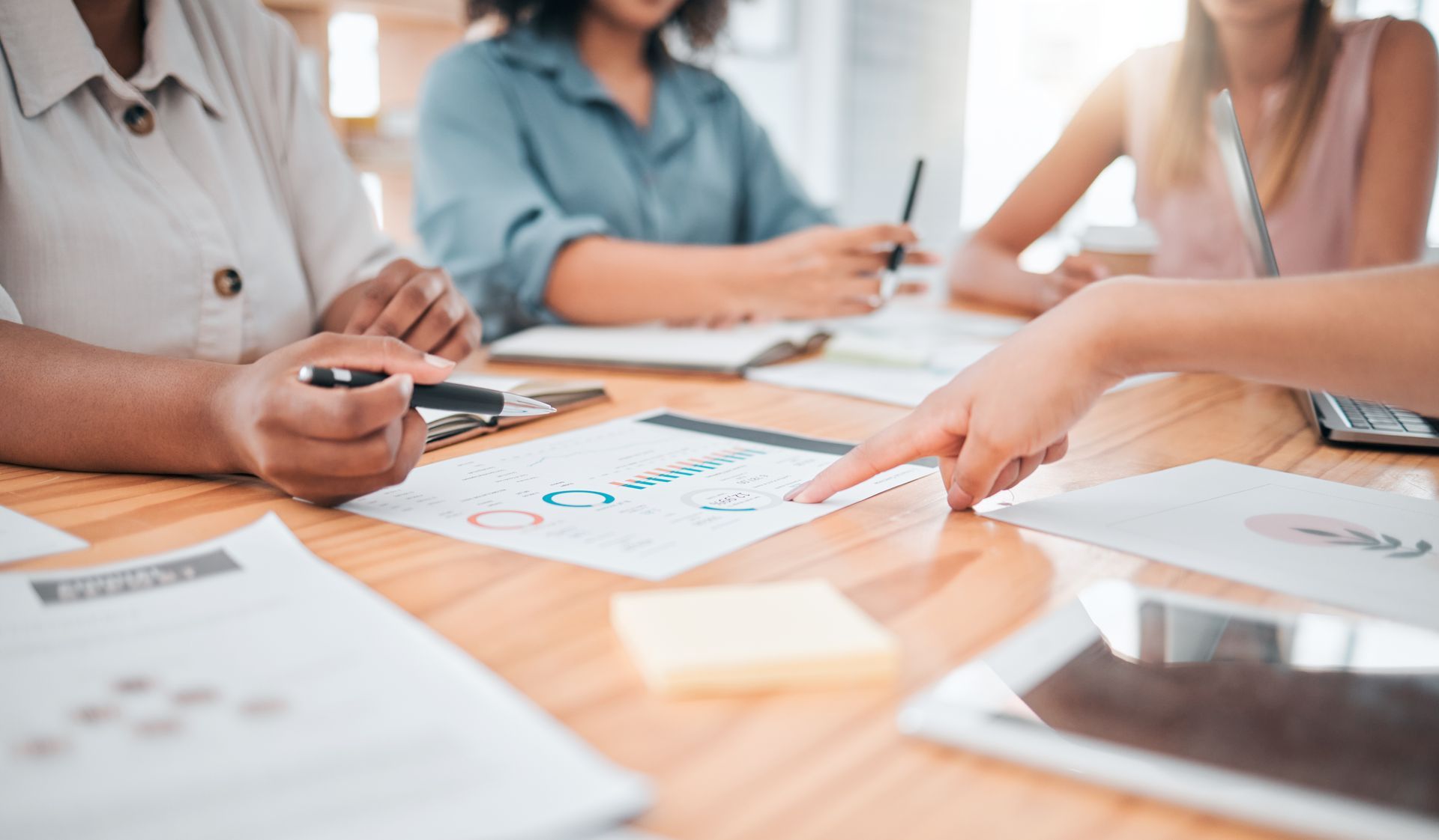 People in a meeting reviewing charts and notes around a wooden table People in a meeting reviewing charts and notes around a wooden table