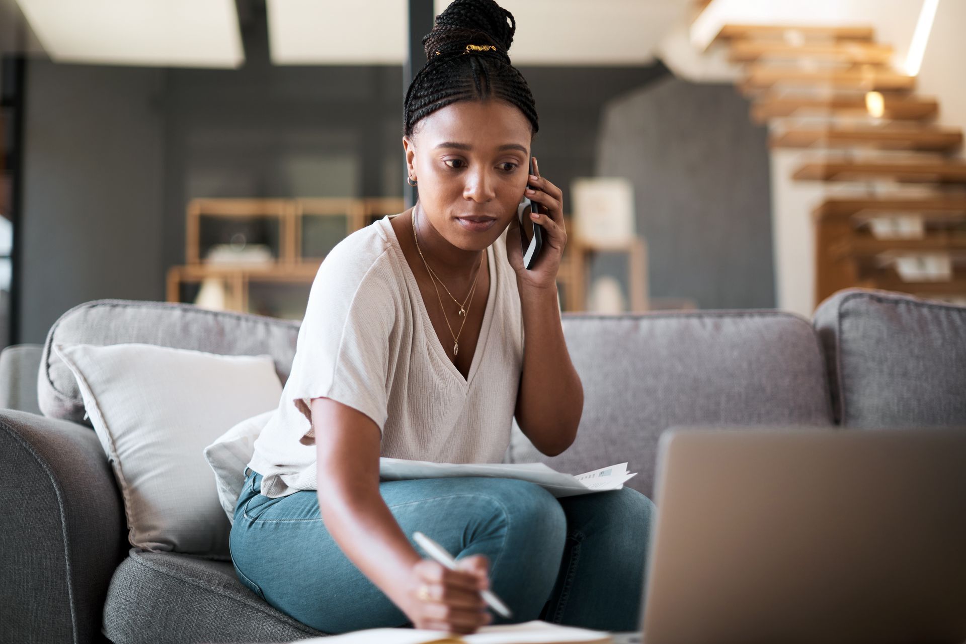 Woman on a gray couch writing while using a laptop in a modern living room. Woman on a gray couch writing while using a laptop in a modern living room.