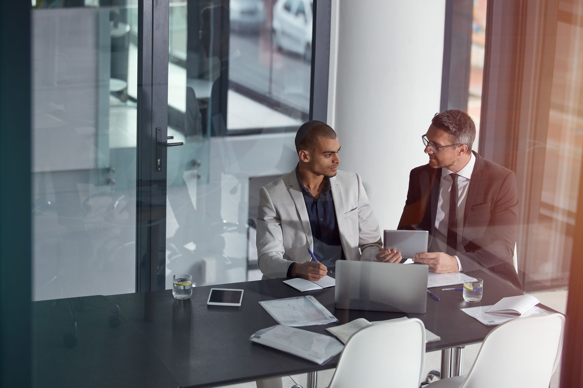 Two coworkers discussing over a laptop at a conference table in a glass-walled office Two coworkers discussing over a laptop at a conference table in a glass-walled office