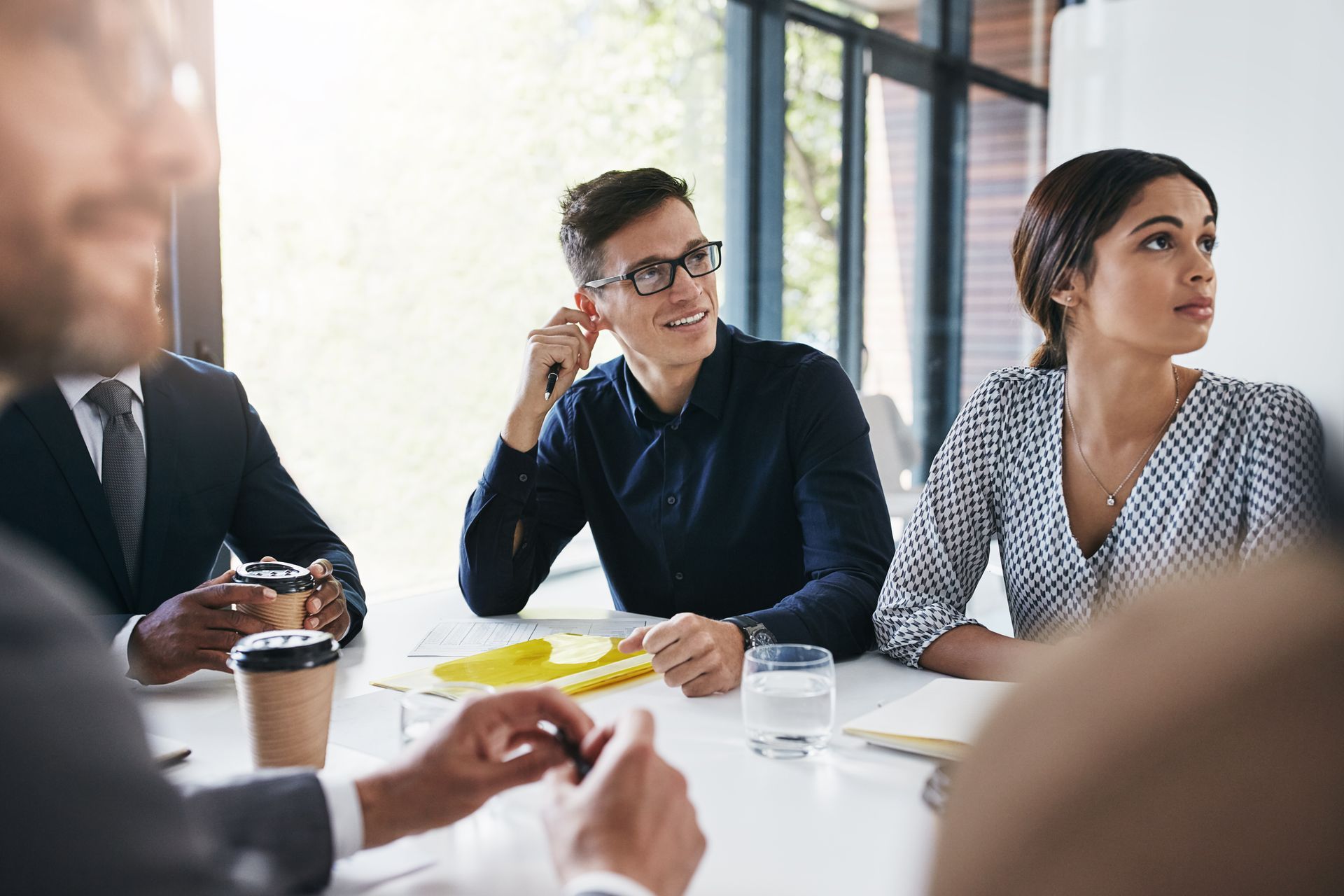 People in a meeting around a table, with papers, coffee, and a laptop in a bright office. People in a meeting around a table, with papers, coffee, and a laptop in a bright office.
