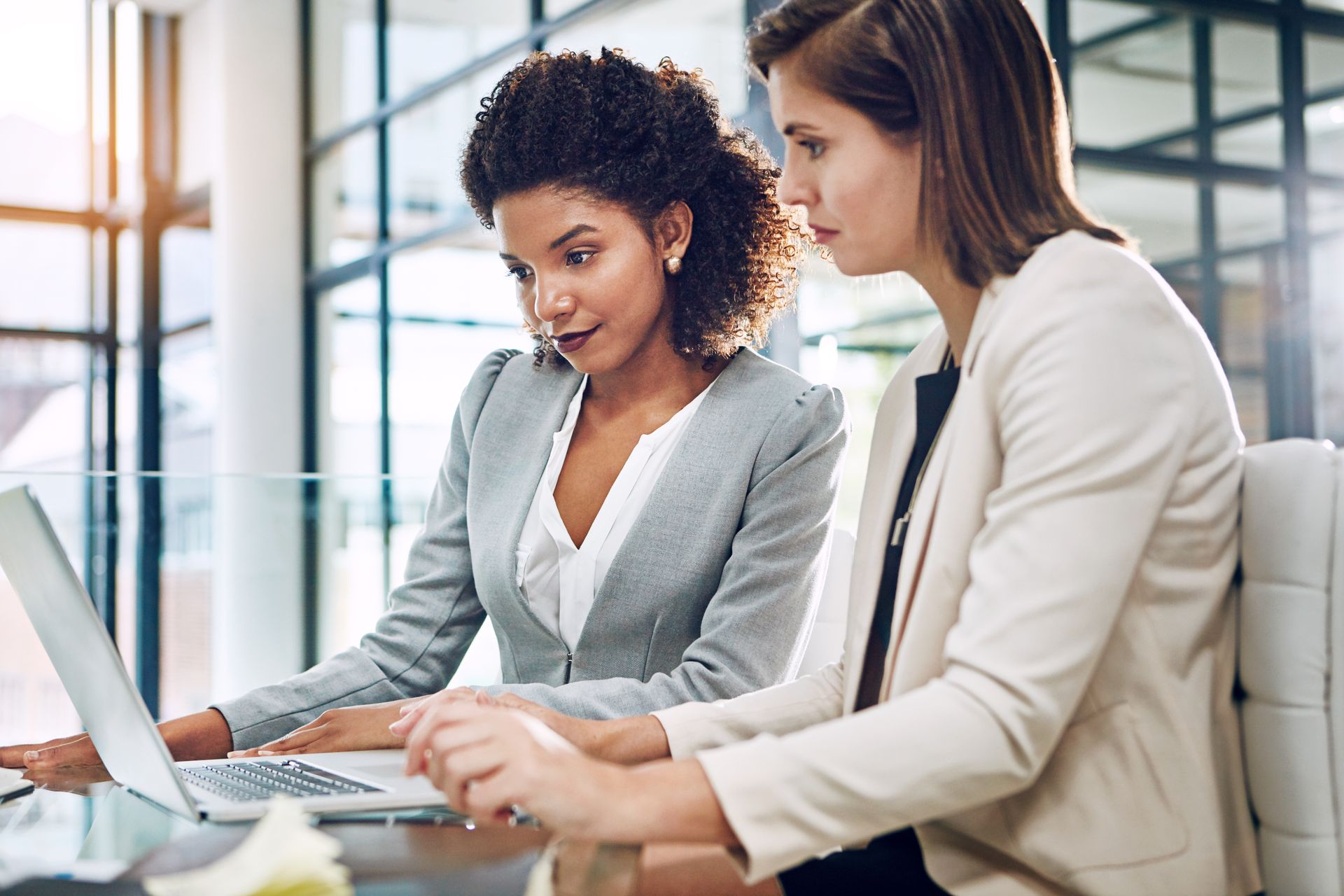 Two coworkers reviewing documents together at a laptop in a bright office Two coworkers reviewing documents together at a laptop in a bright office