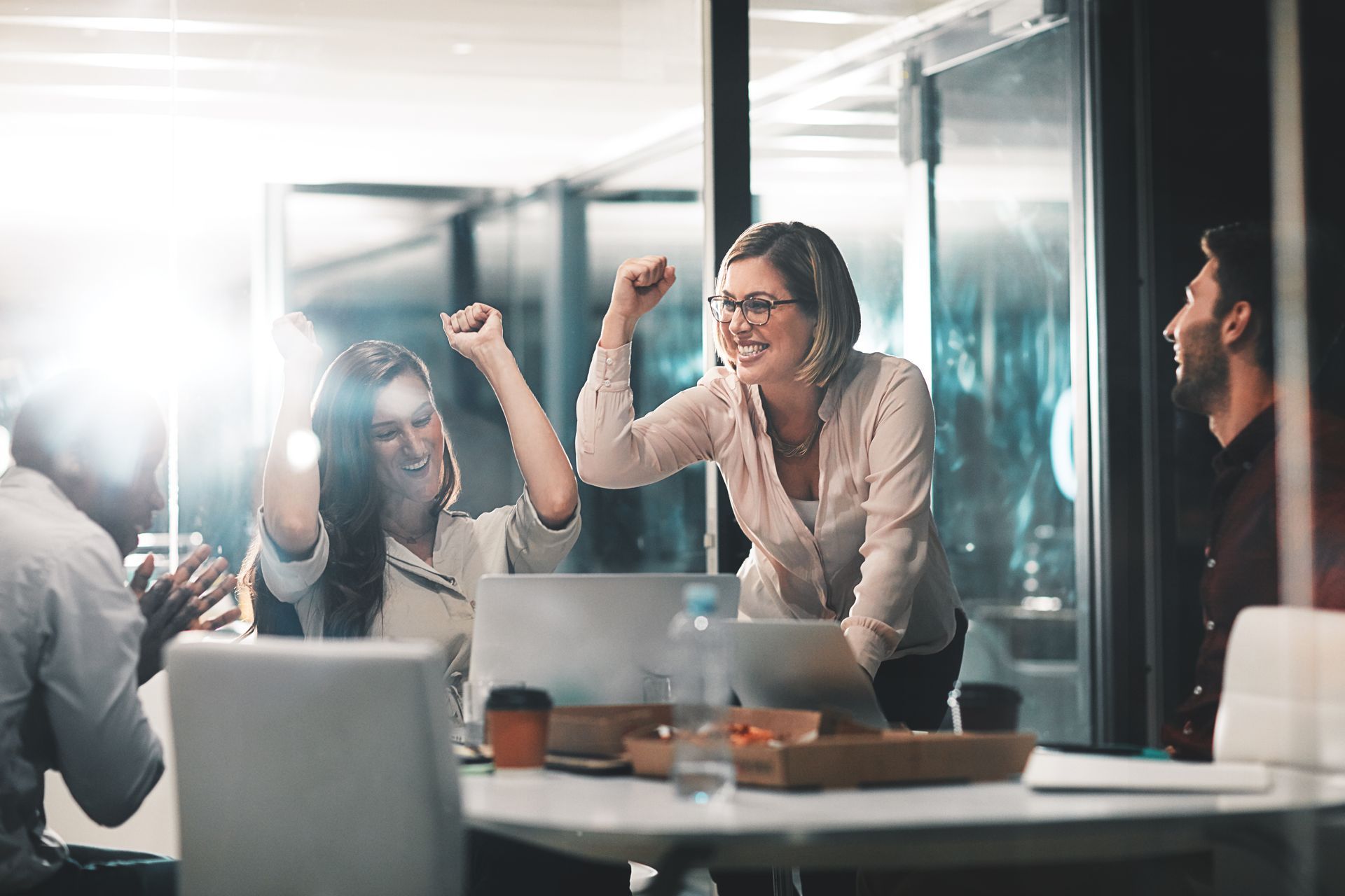 Team meeting with colleagues cheering around a laptop in a bright office conference room Team meeting with colleagues cheering around a laptop in a bright office conference room