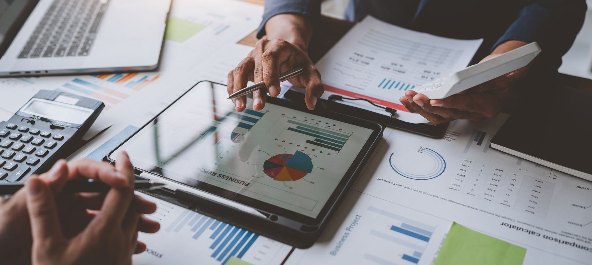 Hands reviewing printed charts and a tablet with analytics in a bright office meeting