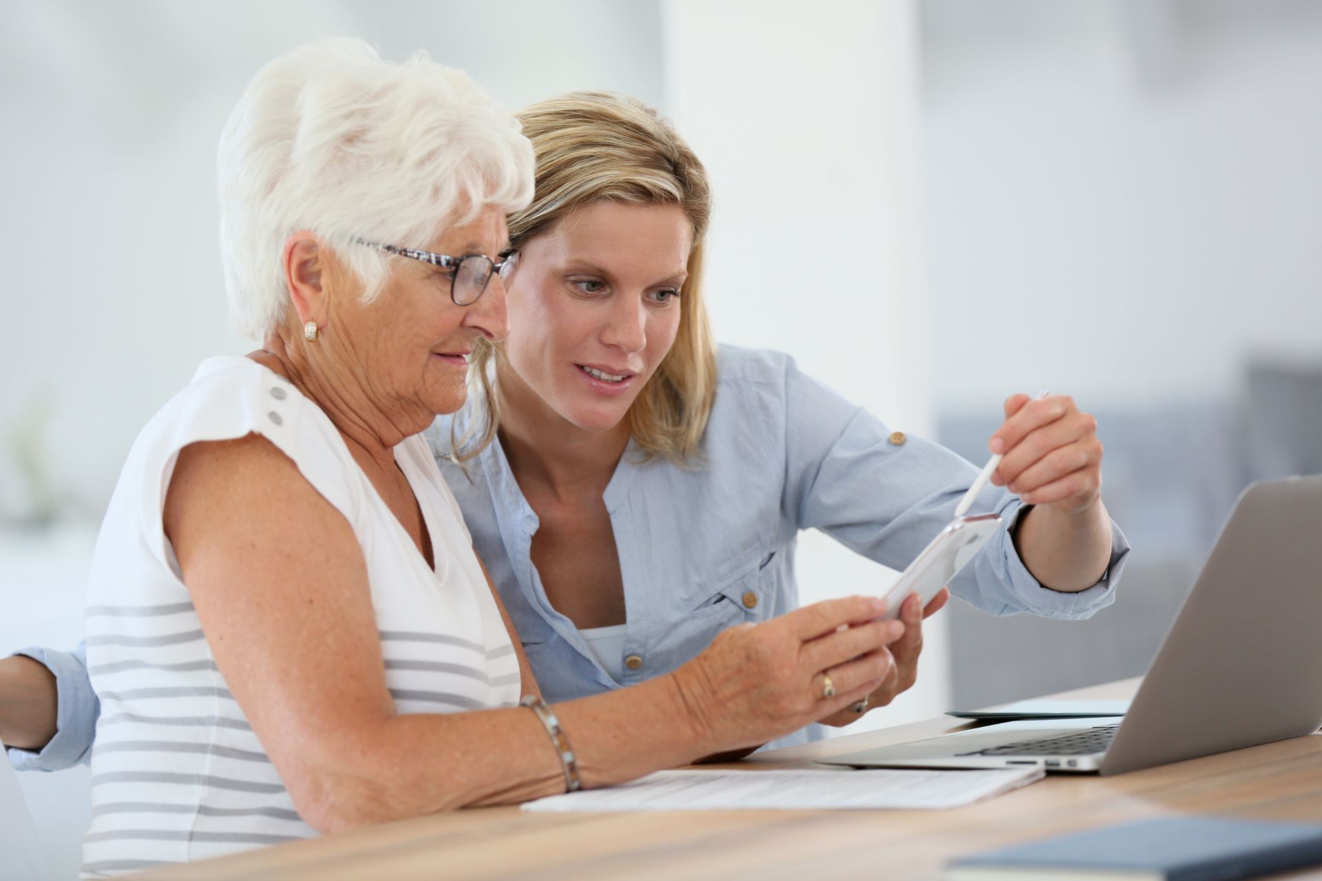 Two women reviewing a document beside a laptop in a bright office Two women reviewing a document beside a laptop in a bright office