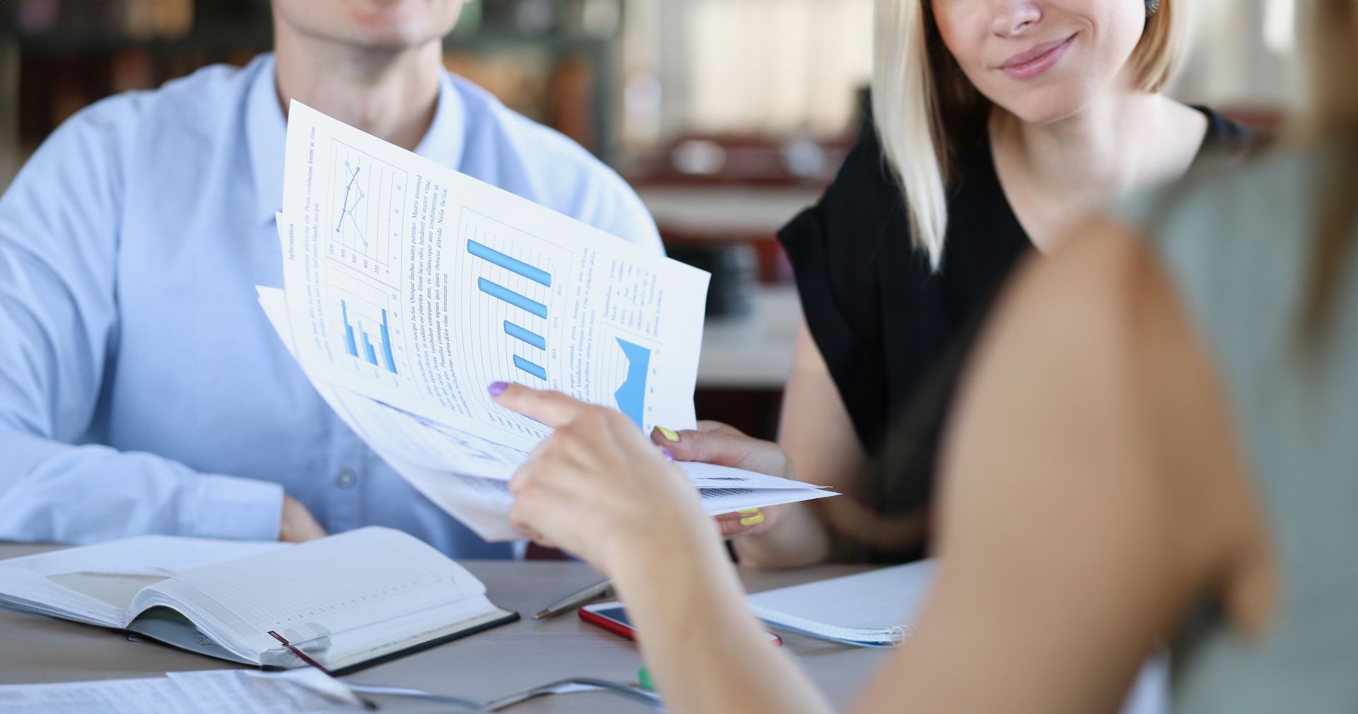 People in a meeting reviewing printed charts and documents at a table People in a meeting reviewing printed charts and documents at a table