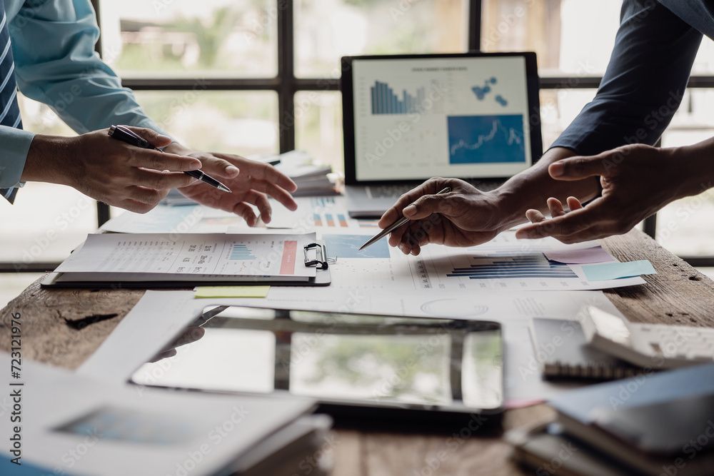 Colleagues pointing at charts during a business meeting with a laptop and papers on the table