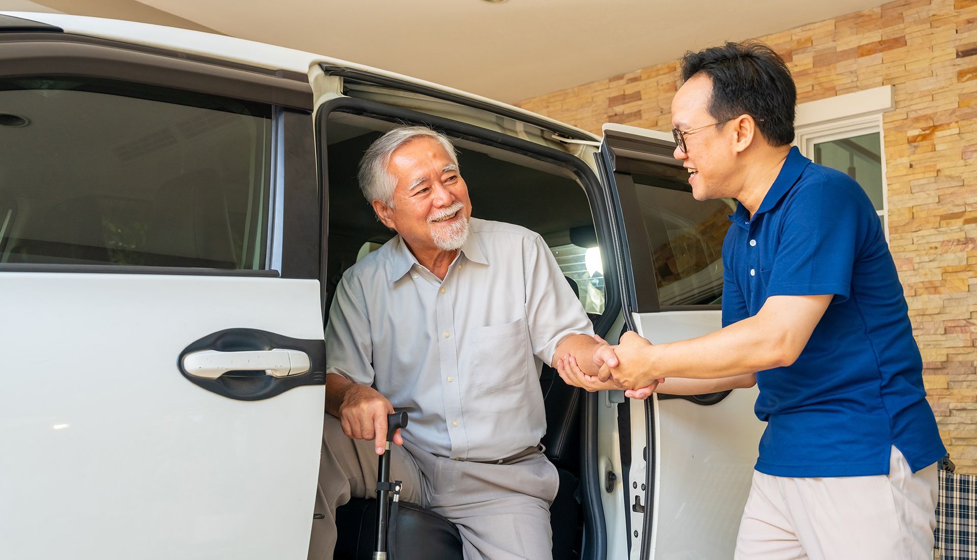 Man assisting another man with a cane out of a white van. They are smiling.