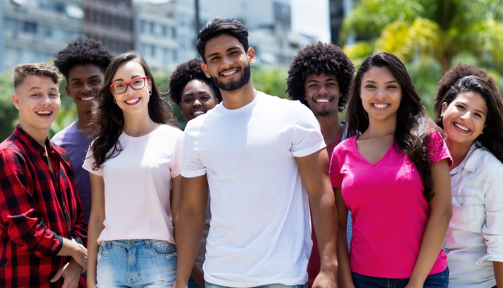 Group of people smiling, standing outdoors. Bright colors, diverse appearances, sunny background.