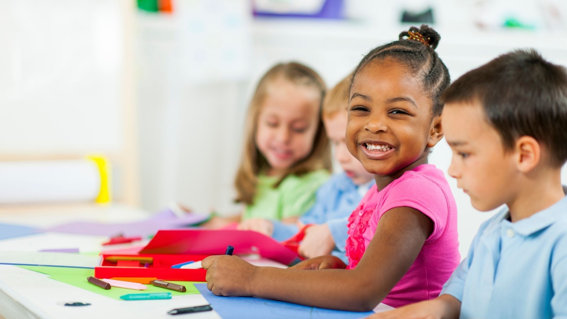 A group of children are sitting at a table in a classroom.