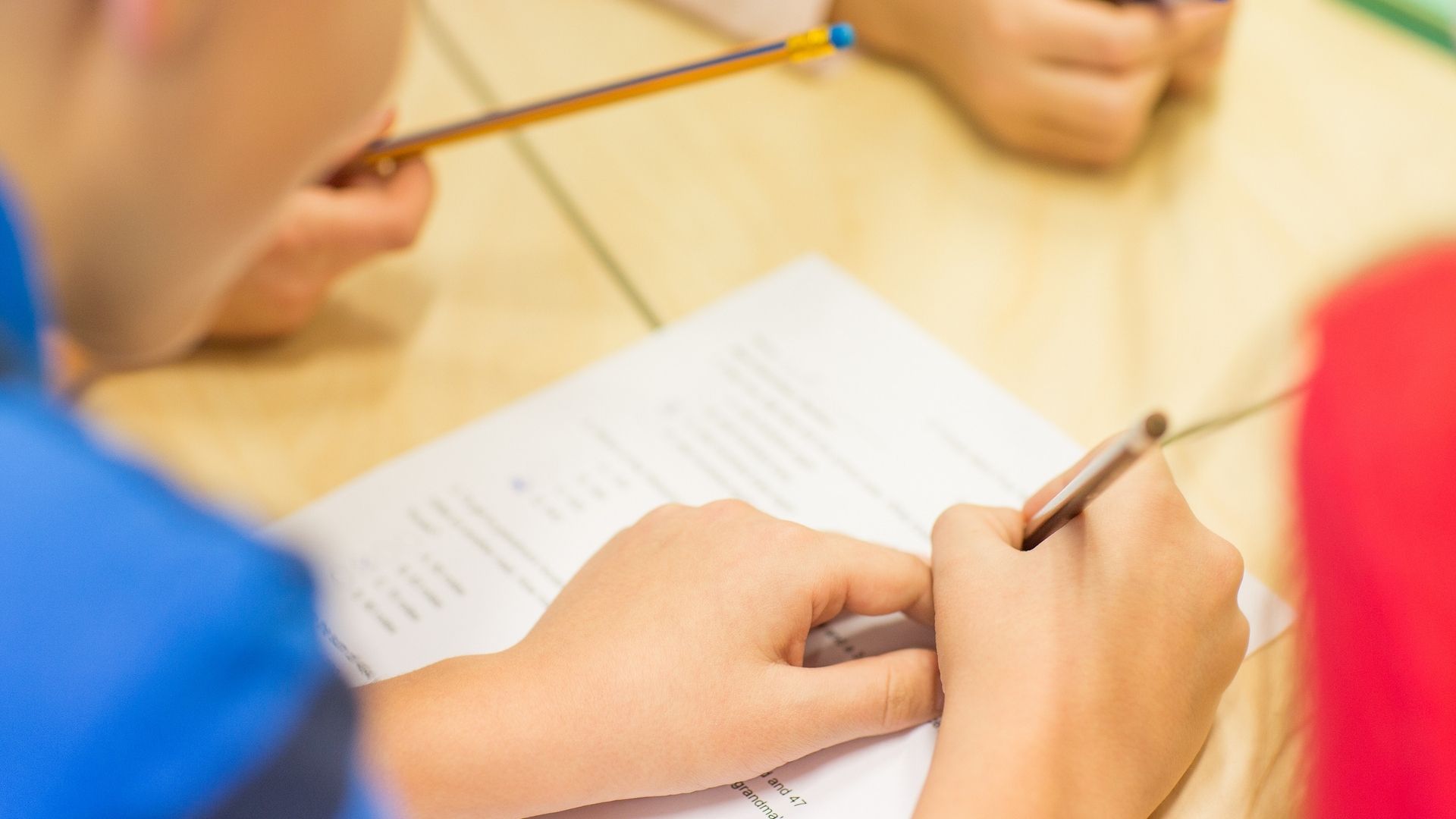 A group of children are sitting at a table writing on a piece of paper.