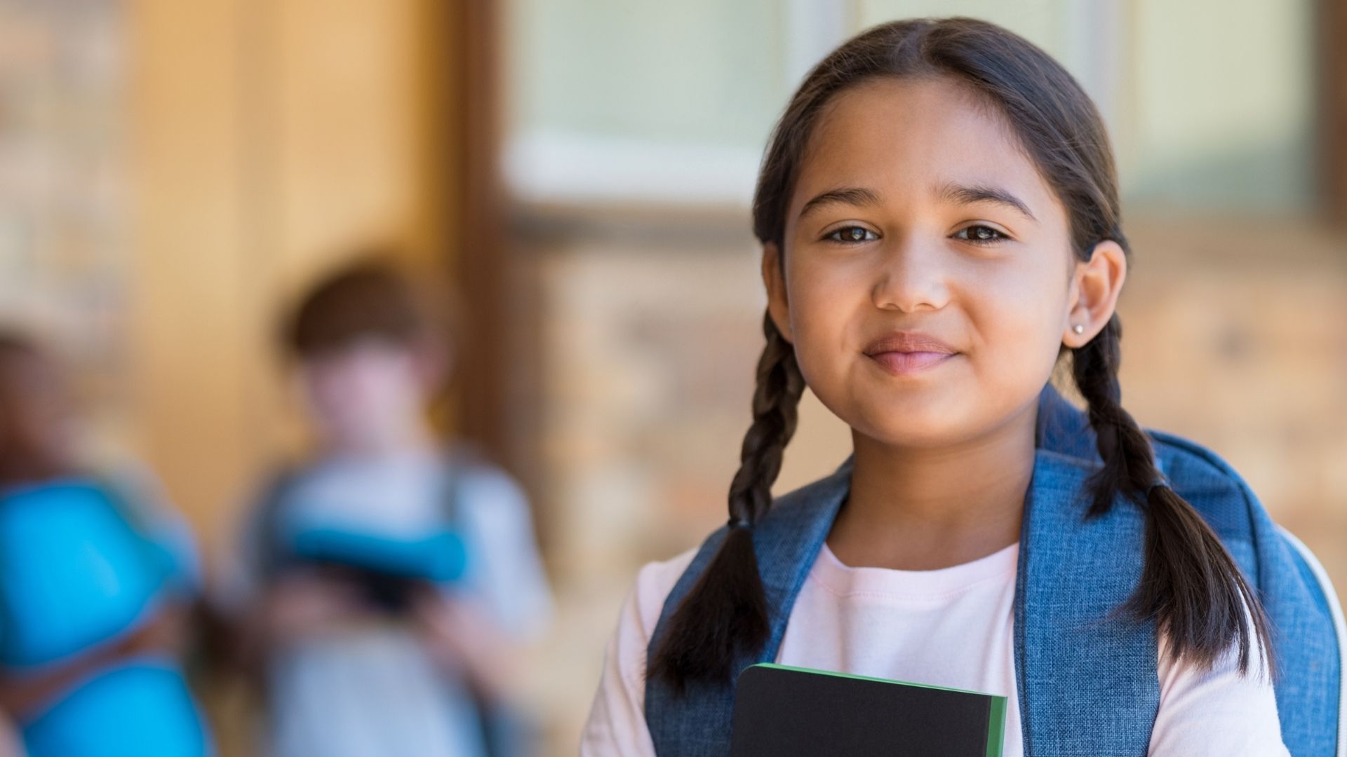 A young girl with pigtails and a backpack is holding a book.