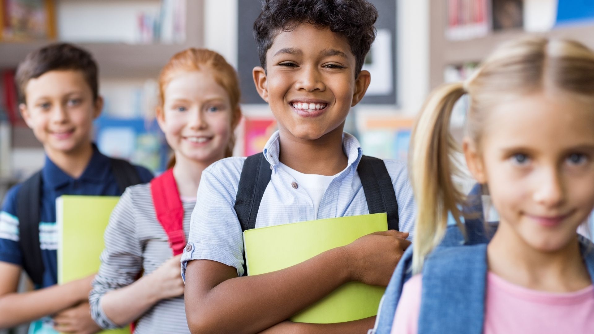 A group of children are standing next to each other in a classroom holding books.