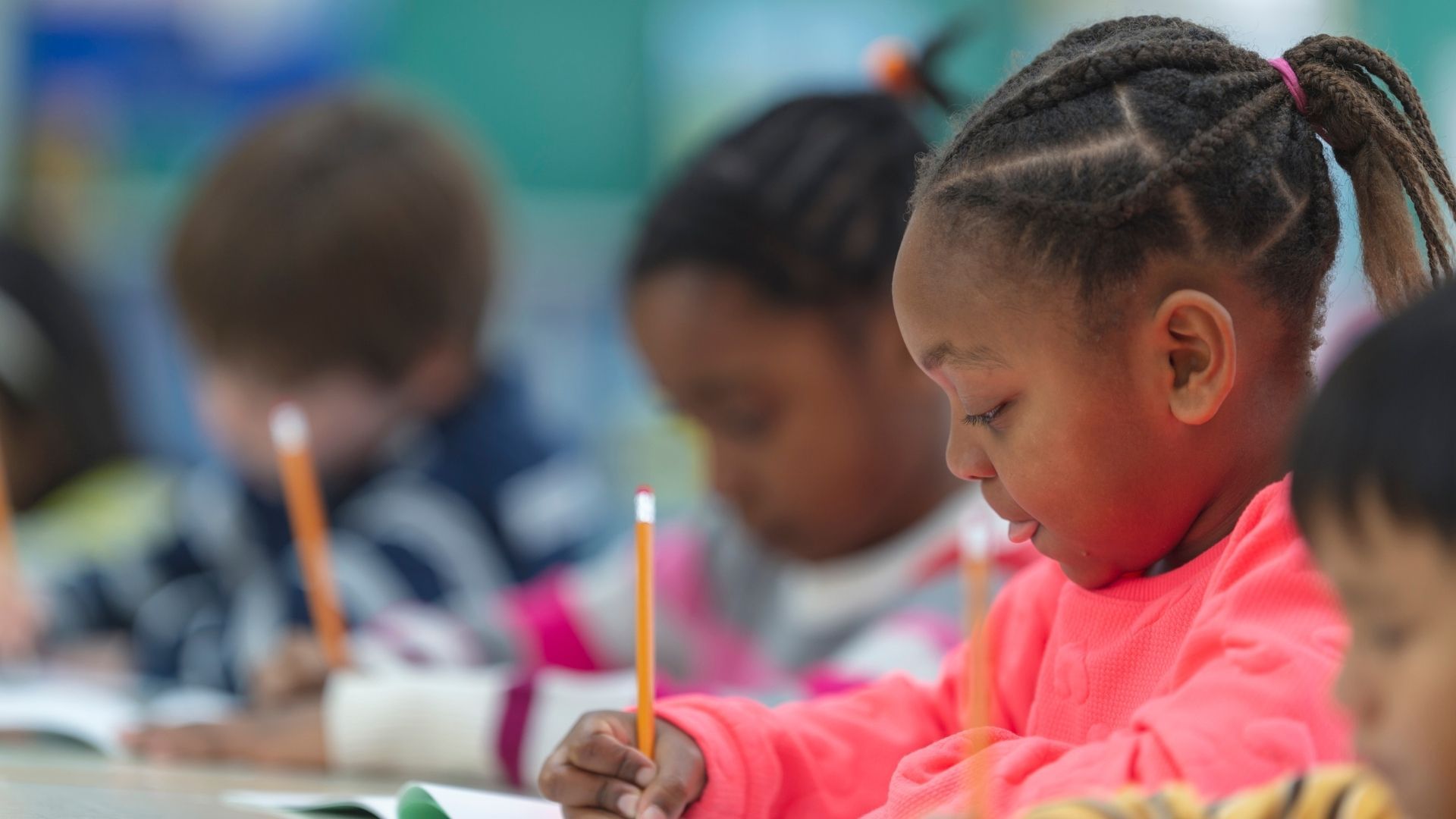 A group of children are sitting at desks in a classroom writing with pencils.
