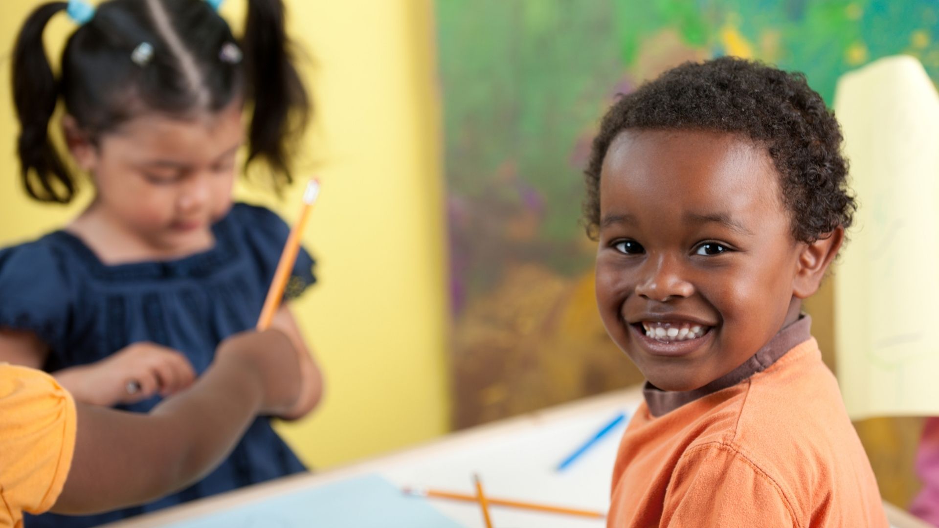 A boy and a girl are sitting at a table with pencils.