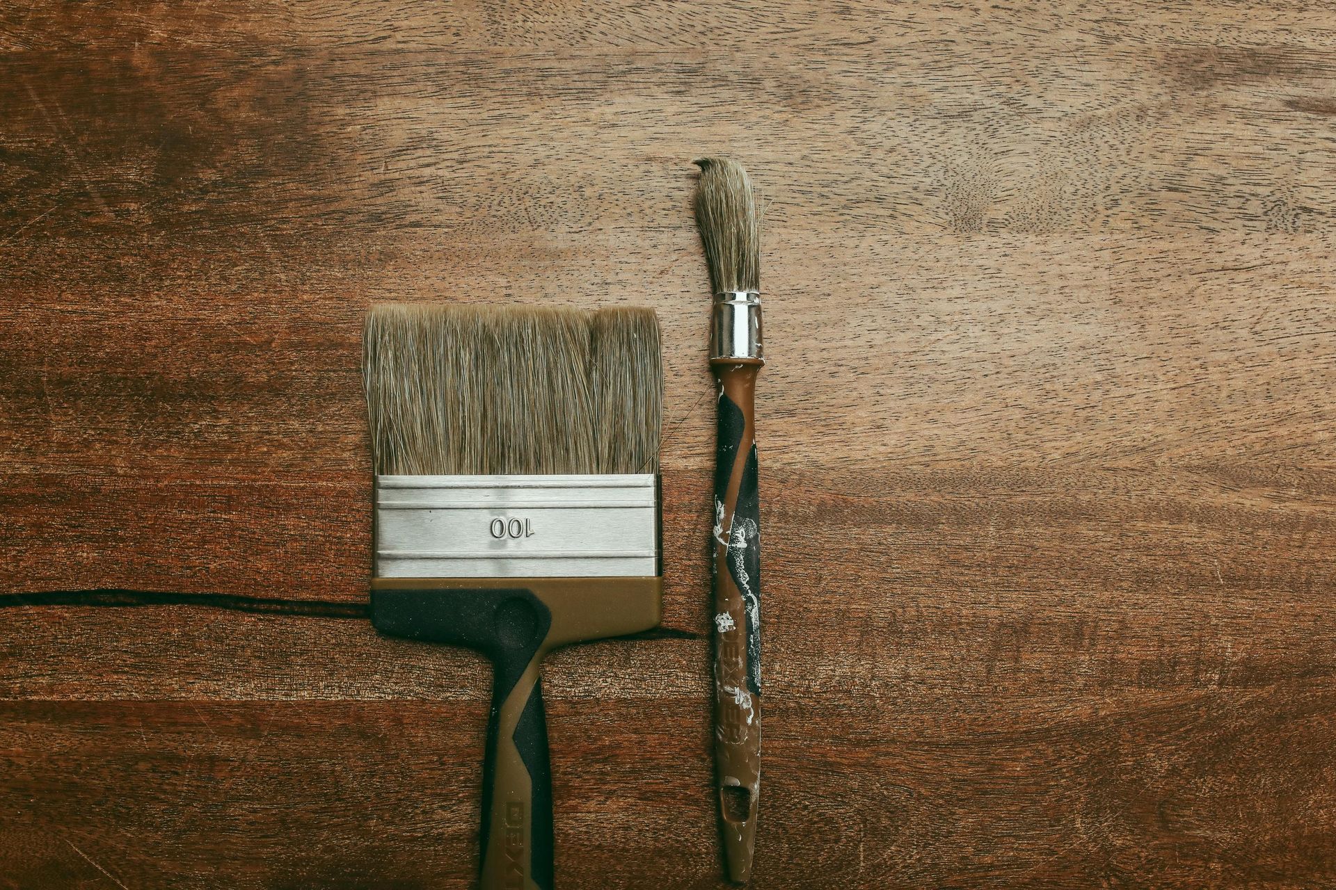 Tre pennelli su una superficie di legno, tra cui un pennello largo e un pennello sottile con della pittura secca.