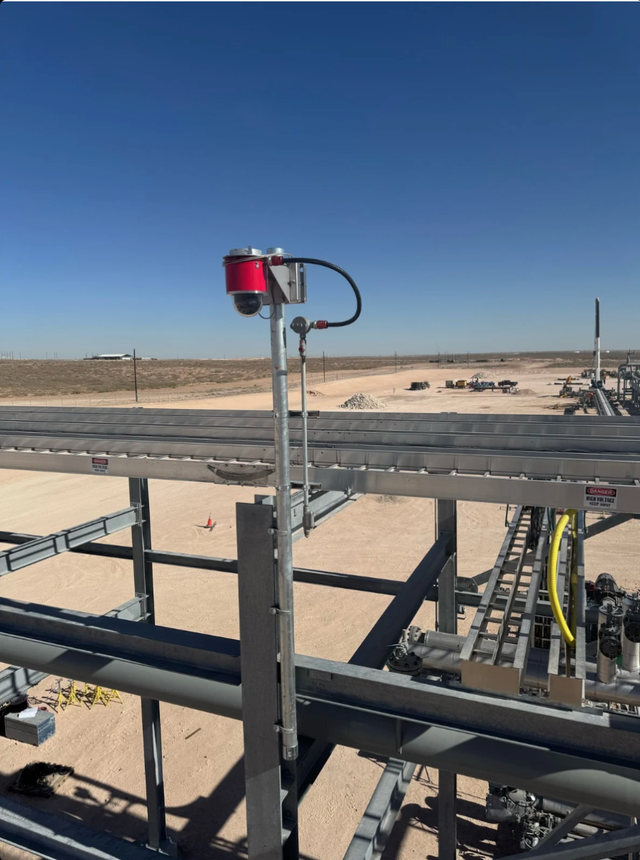 Red sensor on a metal frame at industrial site under a clear blue sky