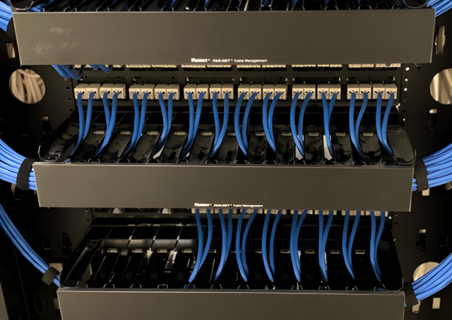 Blue network cables neatly arranged in a black server rack, connecting to patch panels.