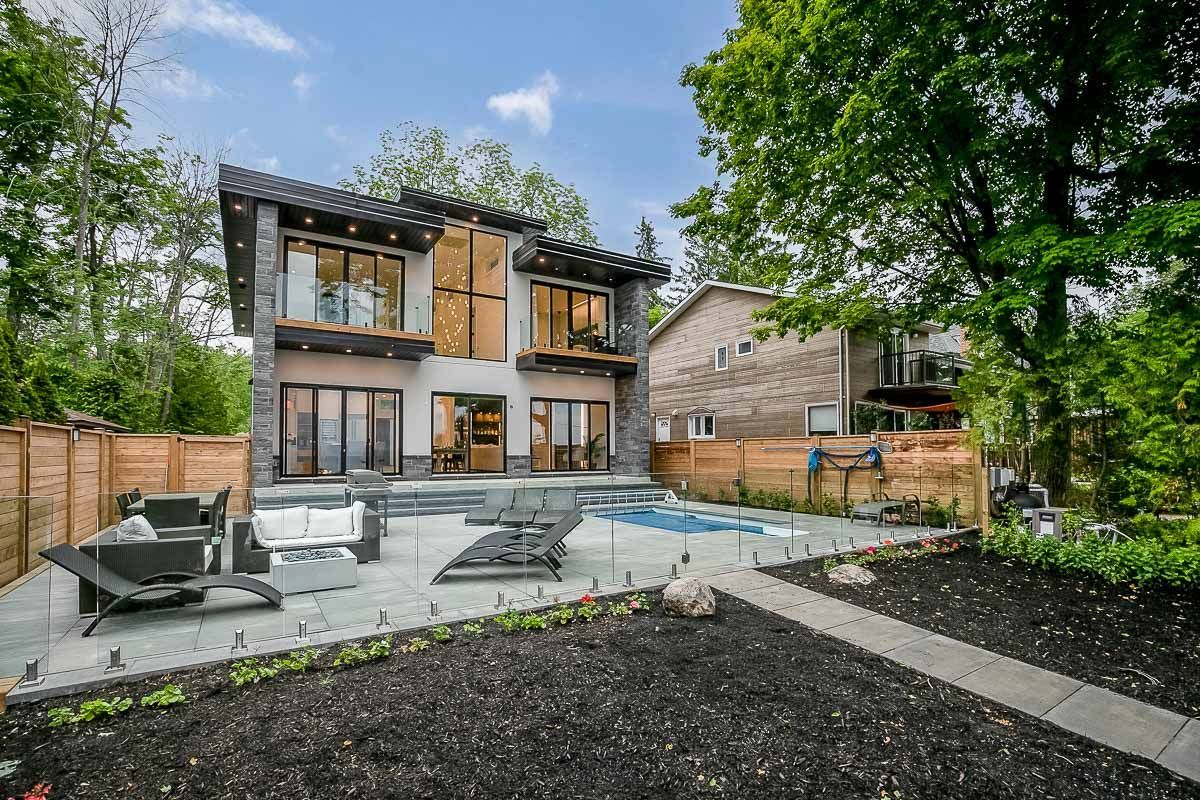 Modern home exterior with stone accents, patio, pool, and surrounding foliage.