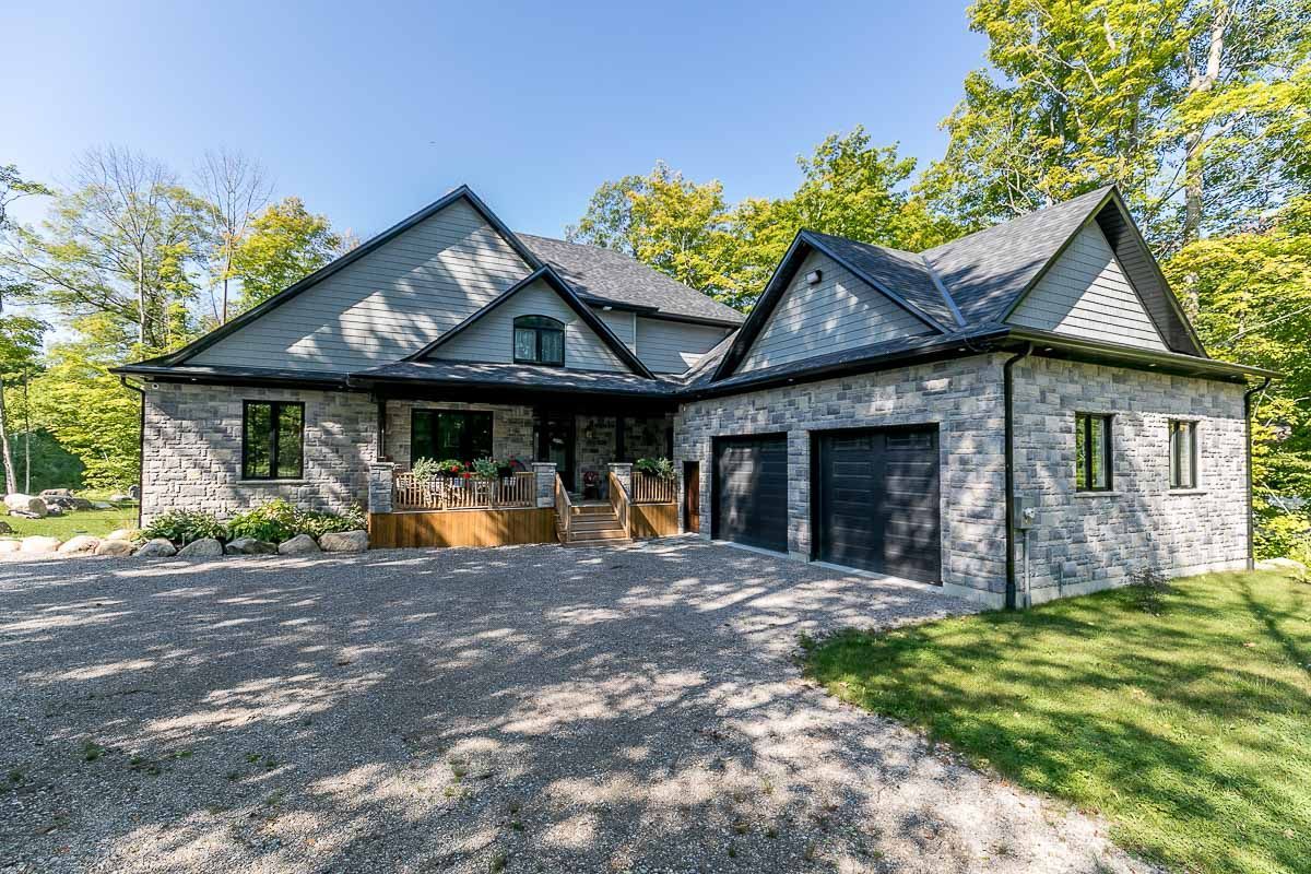 Gray stone house with black garage doors, gravel driveway, and surrounding greenery.