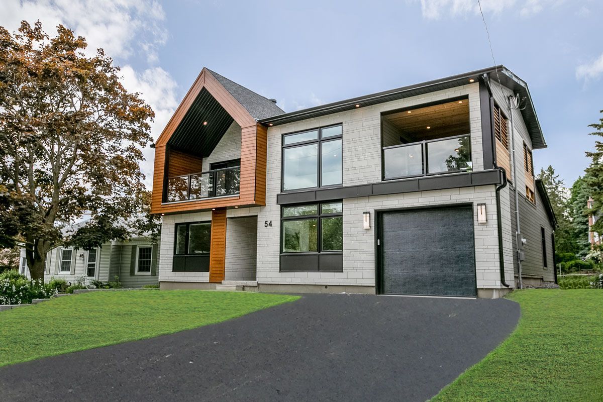 Modern two-story house with black garage door, balcony, and asphalt driveway.