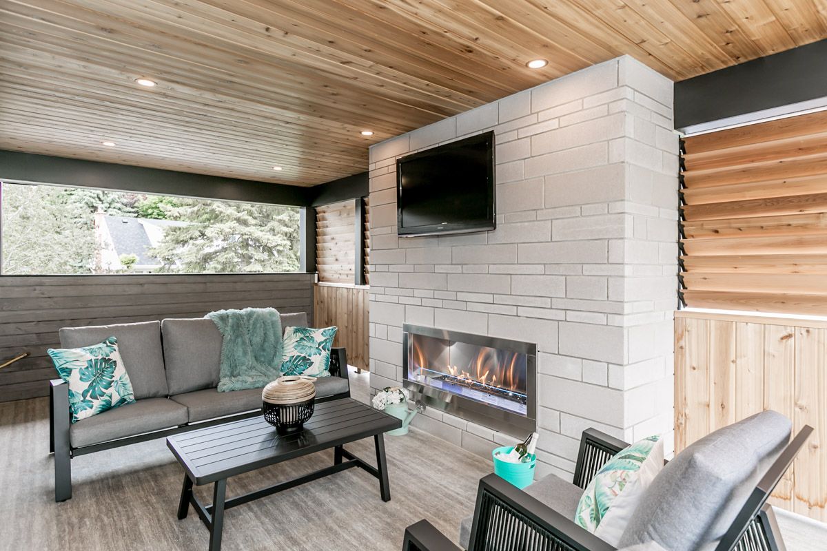 Outdoor living space with sofa, chairs, fireplace, TV, wood ceiling, and neutral colors.