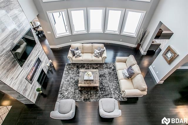 Overhead view of a modern living room with cream sofas, gray rug, and dark wood floors. Large windows and fireplace.