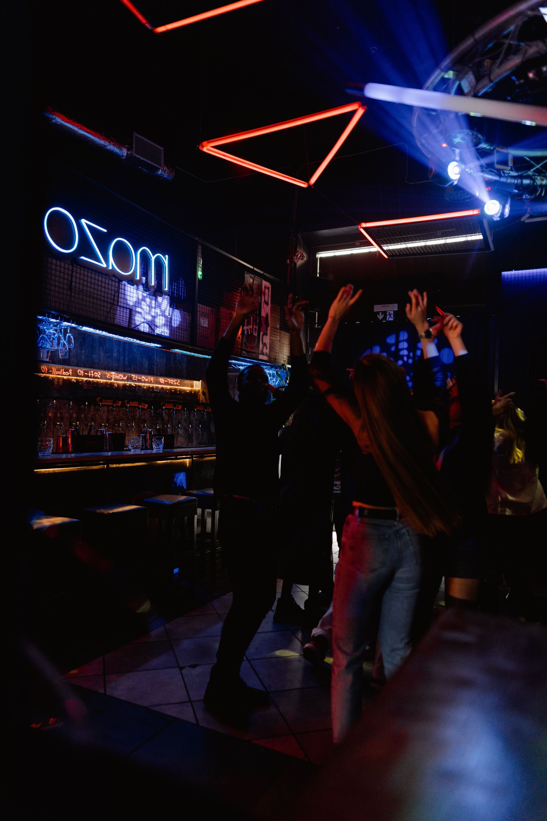 People dancing in a neon-lit nightclub with red geometric ceiling lights