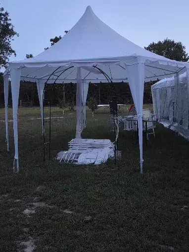 White canopy tent set up on a grassy field at dusk, with a second tent partially visible beside it.