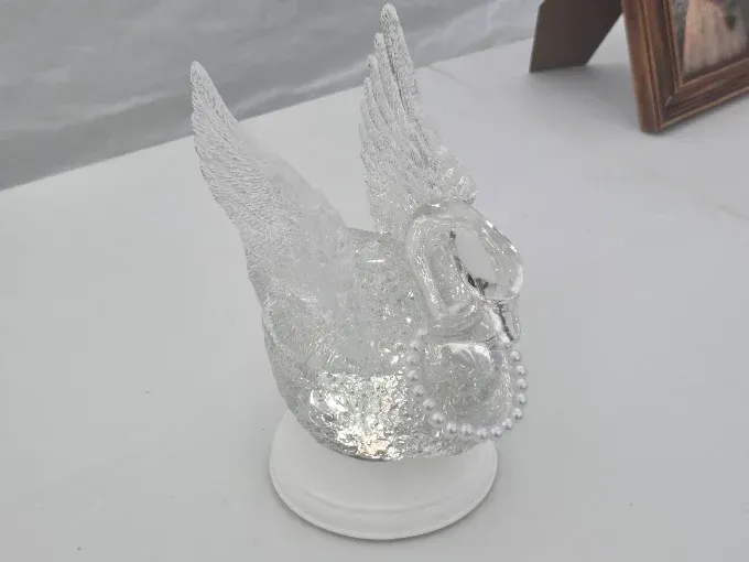 Clear glass angel figurine with raised wings on a white base on a tabletop