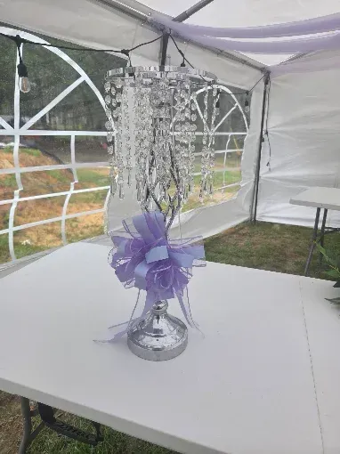 Silver centerpiece with purple ribbon on a white table under a tent for an outdoor event