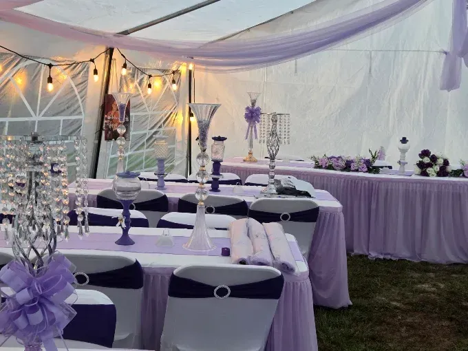 Decorated outdoor wedding reception tent with purple accents and set banquet tables