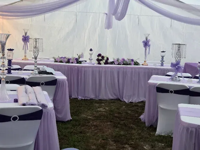 Lavender-decorated tent reception with round tables and white chairs set for an event