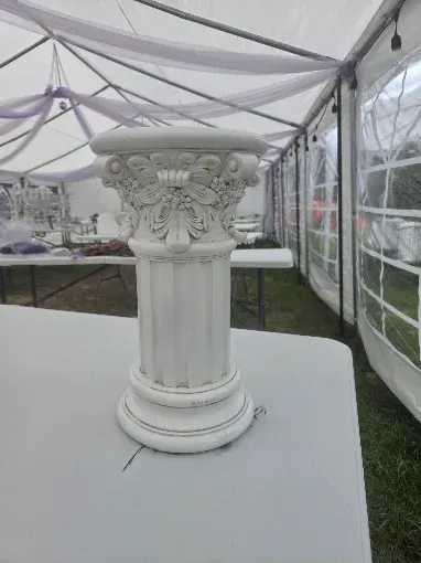 White decorative pedestal table centerpiece under a tent on a white tablecloth.