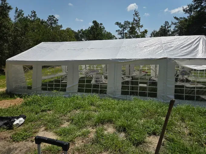 Large white event tent with open windows on a grassy lot beside trees under a clear sky