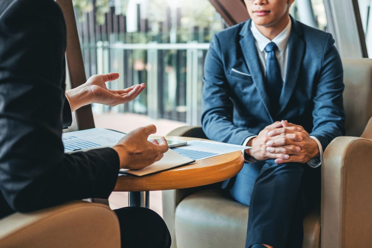 Two people in suits talking across a small table in a bright office lounge