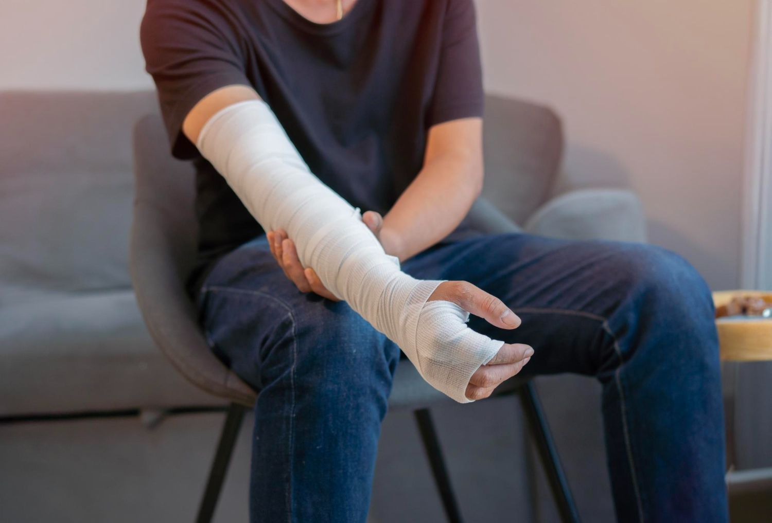 Person with a white cast resting an arm on a chair, seated on a sofa indoors.