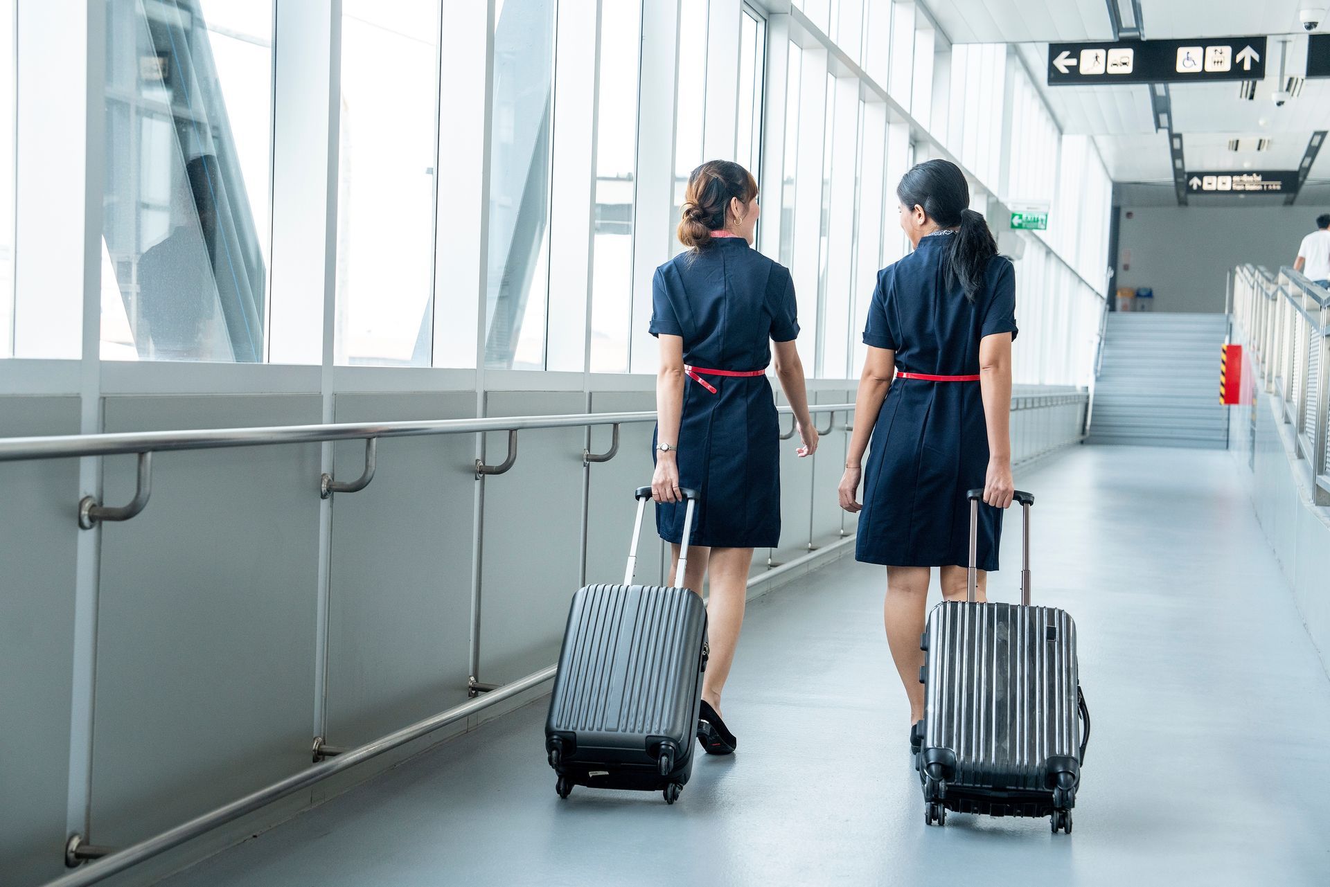 Two hotel staff walking down a bright corridor, each pulling a rolling suitcase