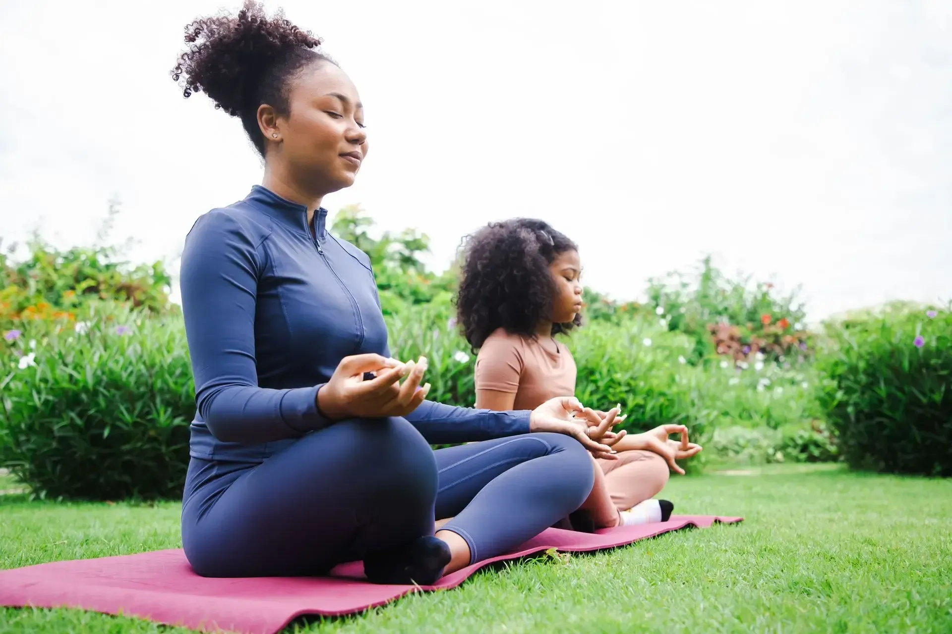 Two people meditating on yoga mats in a grassy park area