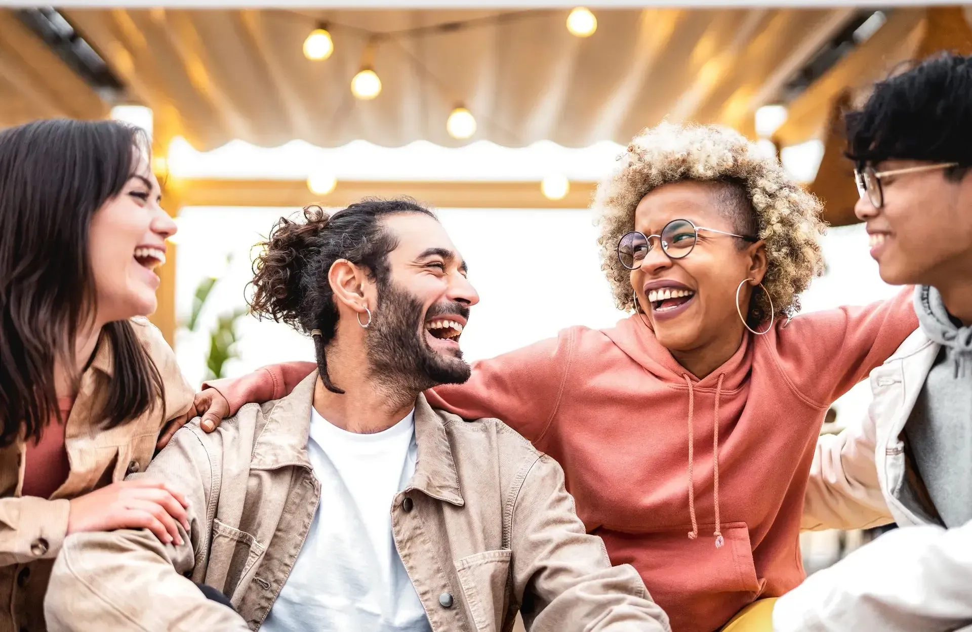 Four friends laughing together in a bright, cozy café lounge