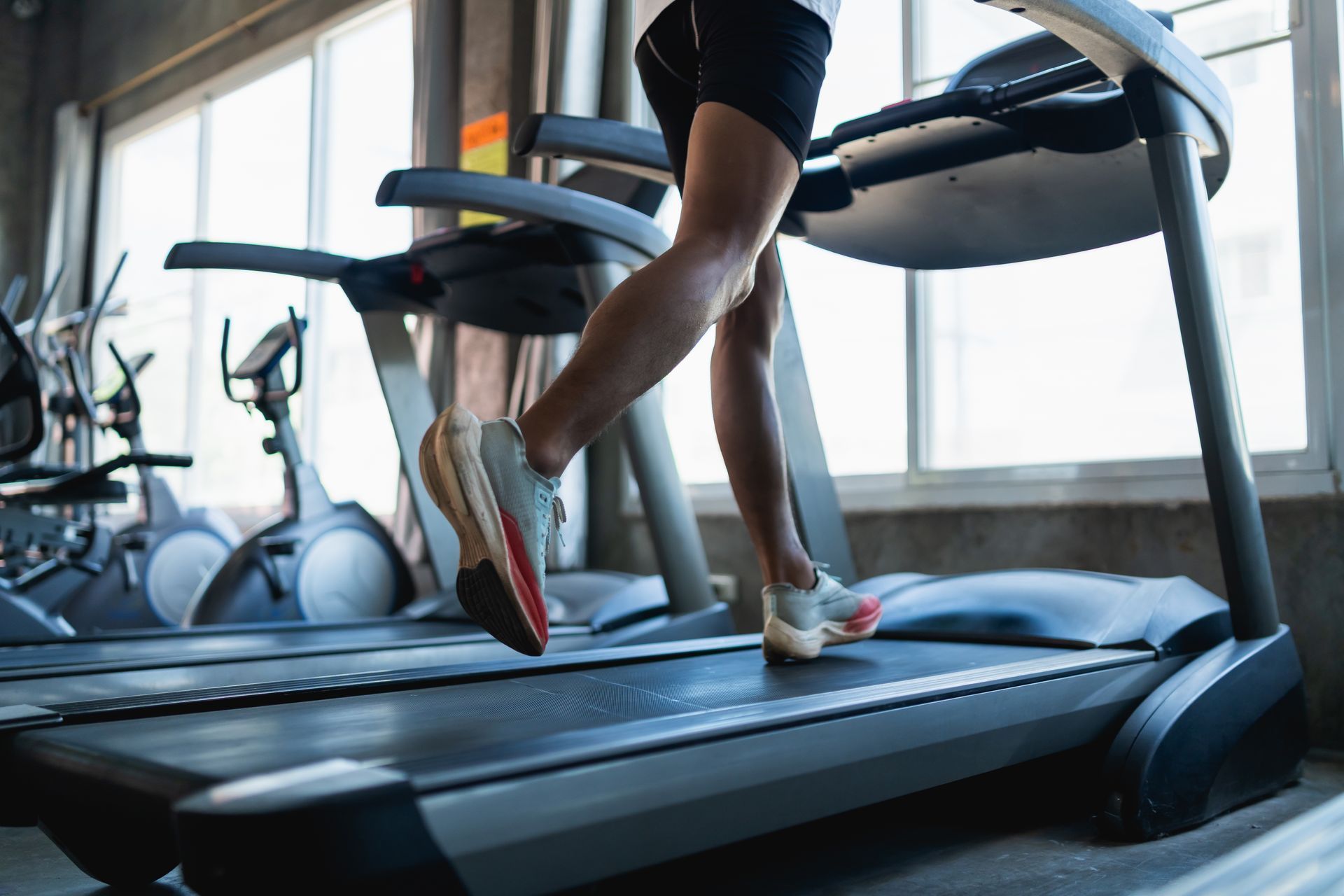Person running on a treadmill in a bright gym, seen from the side.