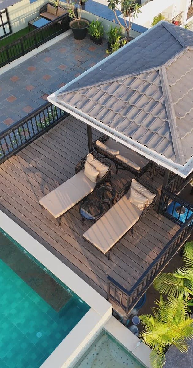 Outdoor poolside deck with a gazebo, two lounge chairs, and a small seating area beside the water.