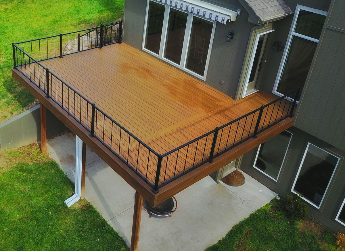Wooden elevated deck with black railing attached to a house, overlooking a grassy yard.