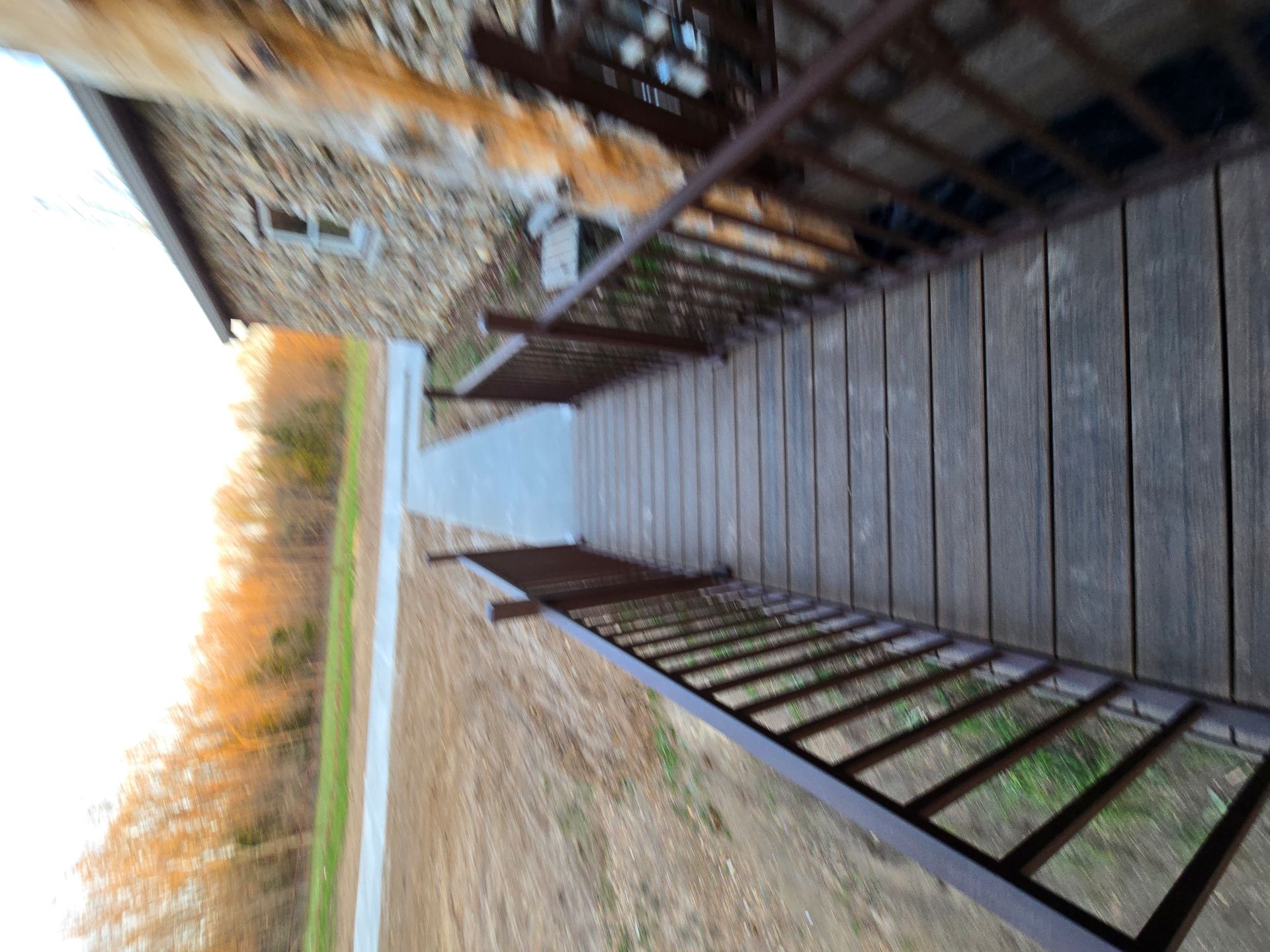 Tilted view of a wooden boardwalk with railing beside tall dry grasses and a fence-like structure