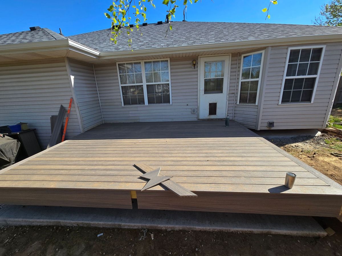 Backyard wooden deck attached to a house, with a sliding door and window.