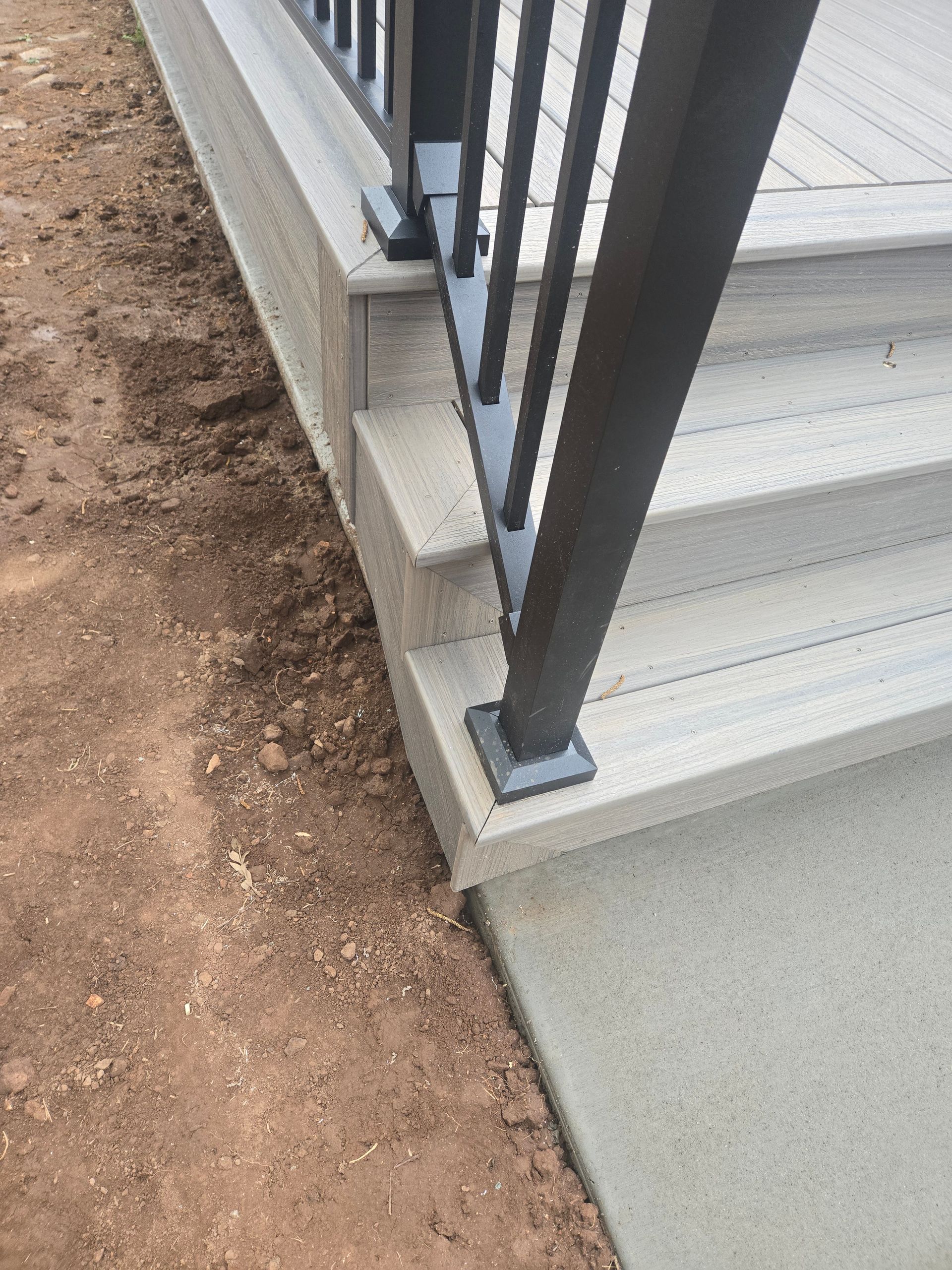 Exterior stair railing on a concrete landing beside a dirt path and white steps