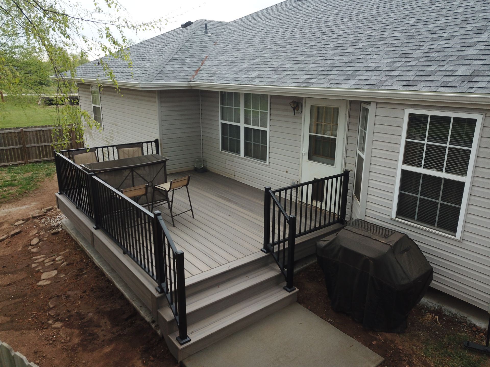 Back porch deck with black railings, gray siding, and covered grill beside steps