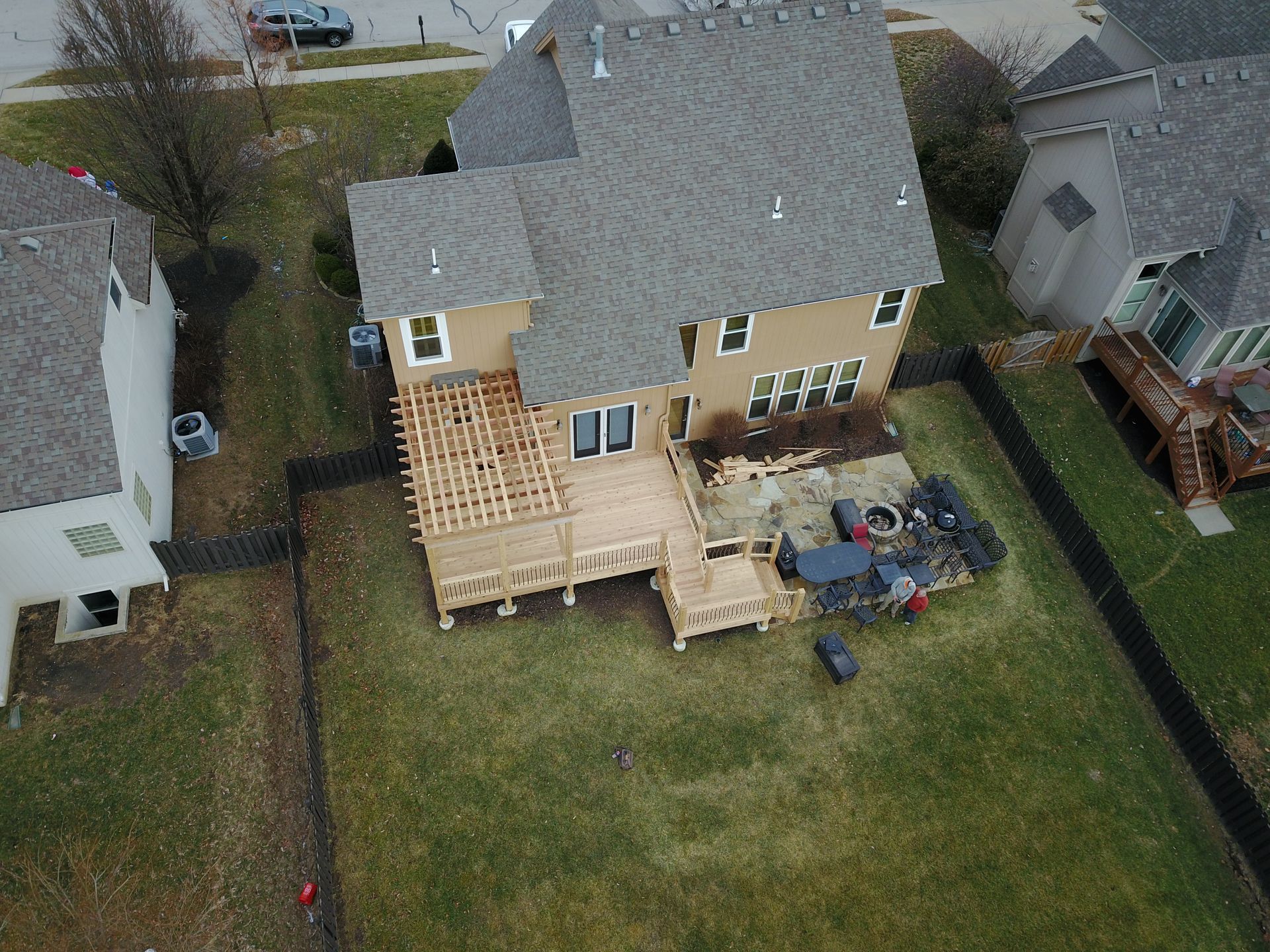 Aerial view of a house with a large wooden deck under construction in a fenced backyard