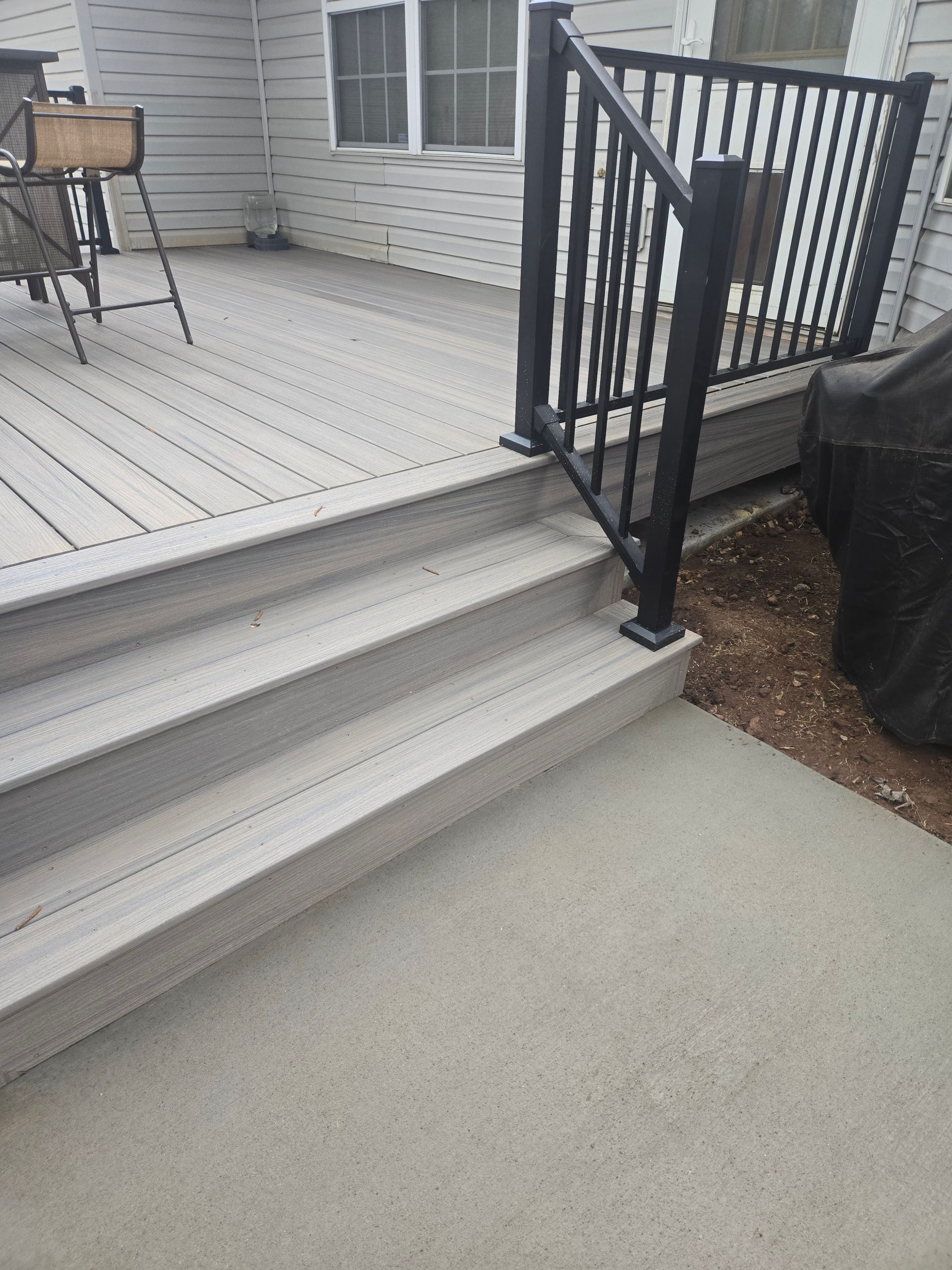 Gray steps leading to a white deck with black railing and a chair on the porch.