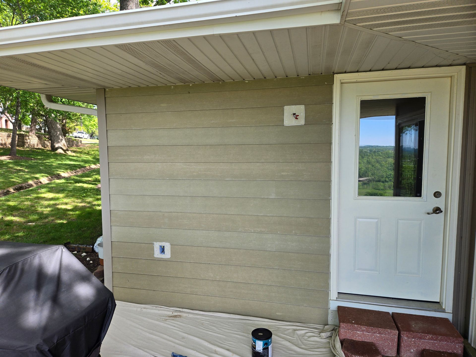 Small beige house entry with white door, covered porch, and green yard reflected in the glass.