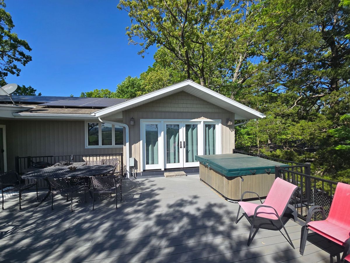 Patio outside a house with outdoor seating, hot tub, and trees under a blue sky